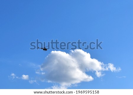small silhouette of helicopter against big white cloud on blue sky Royalty-Free Stock Photo #1969595158