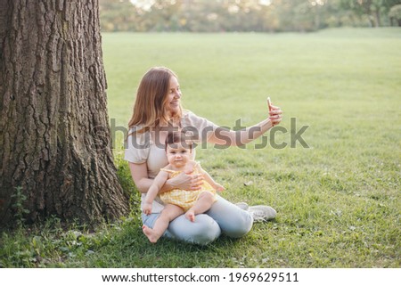 Mothers Day. Happy family. Middle age smiling Caucasian mother with girl toddler daughter taking photo selfie with smartphone camera in park. Mom embracing child baby on summer day outdoor. 