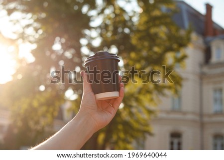 Black paper cup with coffee in woman hand. Time for drinking coffee in the city. Disposable paper cup closeup. Blank space for text, mockup. Concept of coffee to go, takeaway drinks, morning snack.