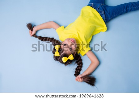 Cute little girl Indian girl with long hair in a yellow T-shirt lies on a blue background, view from above, space for text