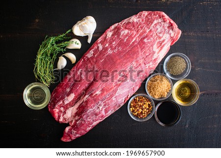 Bourbon Marinated Grilled Flank Steak Ingredients: Raw flank steak, herbs, and other ingredients on a dark wood background
