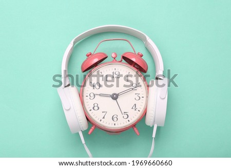 Stereo headphones with pink alarm clock on blue background. Minimalism music concept. Creative layout. Fresh idea.
