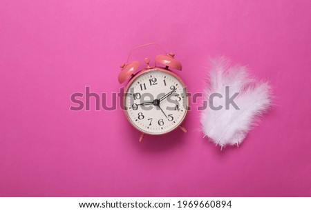 Soft feathers and alarm clock on pink background. Minimalism. Top view. Flat lay