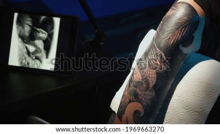 Close up photo of man doing tattoo of snake for woman in studio