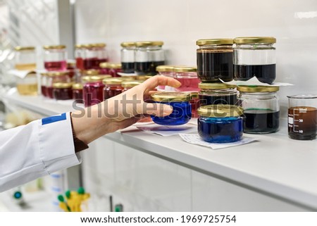 the hand of a chemical laboratory worker puts a jar with a blue drug on the shelf with liquids of different colors on the shelf