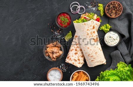 Shawarma with vegetables, salad and chicken on a black background with ingredients. Top view, copy space. Royalty-Free Stock Photo #1969743496