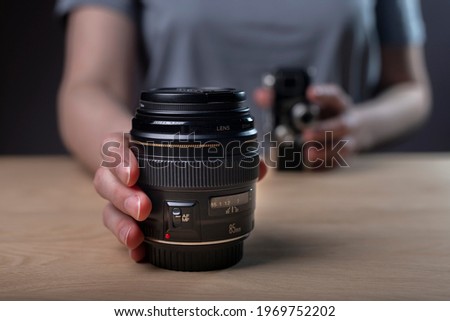 Photographer showing camera lens, blurred vintage old one and modern 85 mm lens in focus. Royalty-Free Stock Photo #1969752202