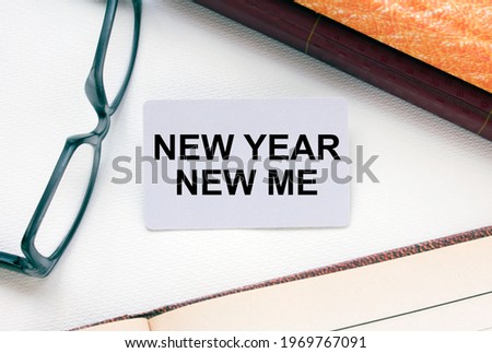 Text New Year New Me on a business card lying next to notepad with eyeglasses and text documents. Business concept