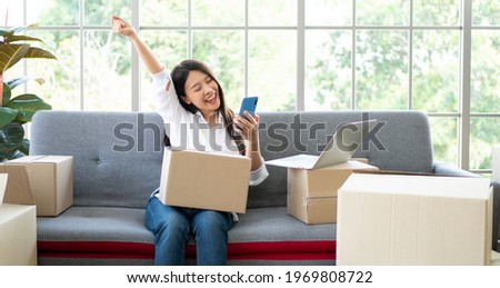 Happy young Asian woman entrepreneur, Smile for sales success after checking order from online shopping store in a smartphone at home office, Concept of merchant business online and eCommerce Royalty-Free Stock Photo #1969808722