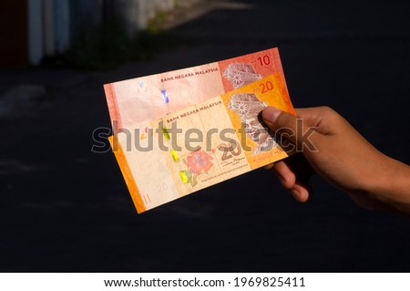Asian child's hand holding 10 and 20 Ringgit Malaysia money, shallow focus, on dark background