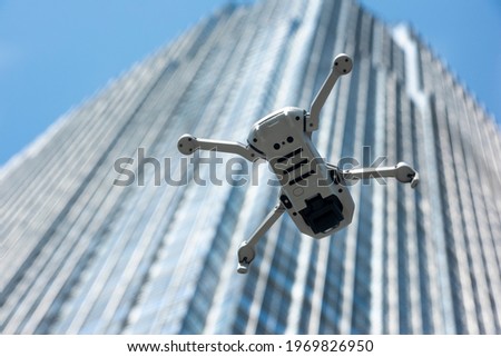 A drone flying across the sky with a large skyscraper in the background. 