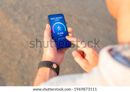 Man using daily activity tracking app on mobile phone showing 10 000 steps daily goal achievement Royalty-Free Stock Photo #1969873111