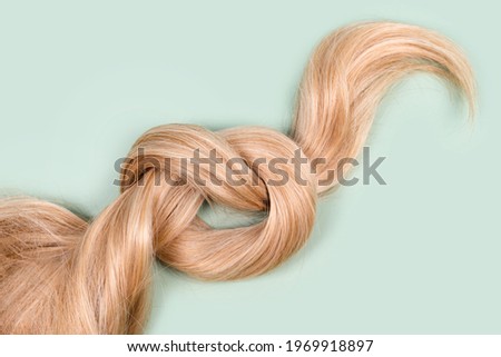 Blonde hair lock tied in knot. Strand of honey blonde hair on mint background, top view. Hairdresser service, hair strength, haircut, hairstyle, dying or coloring, hair extension, treatment concept Royalty-Free Stock Photo #1969918897
