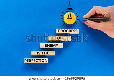 Perfection or progress symbol. Wooden blocks on blue background, copy space. Light bulb icon. Businessman hand with pen. Words 'Perfection is the enemy of progress'. Progress concept. Copy space. Royalty-Free Stock Photo #1969929895