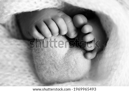 Feet of a newborn with a wooden heart, wrapped in a soft blanket. Black and white studio photography.