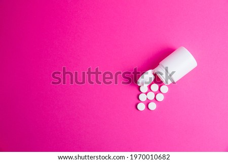 Flatley, white pills and jar on pink paper background copy space.