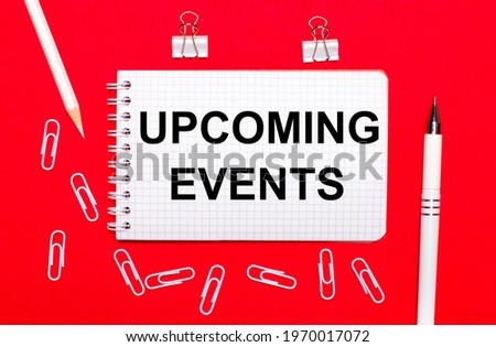 On a red background, a white pen, white paper clips, a white pencil and a notebook with the text UCOMING EVENTS. View from above