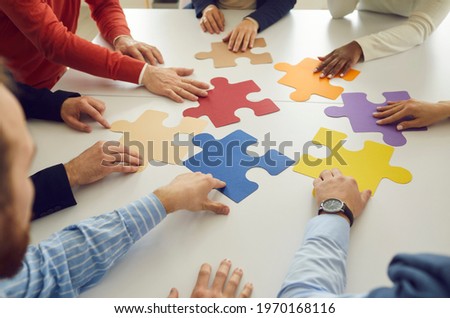 Close up of hands of multiracial businessmen sitting in a circle at a table making up pieces of a colored puzzle. Team is looking for a way to solve the problem, find a way out of a difficult Royalty-Free Stock Photo #1970168116