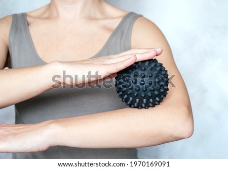 A young woman massages her elbow with spiky trigger point ball, tennis elbow exercises Royalty-Free Stock Photo #1970169091