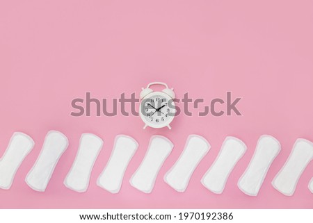 Daily pads and white alarm clock on pastel pink background. Concept of women's health and regular periods. Copy space
