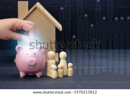 wooden family figurines and pink ceramic piggy bank on blue background. Concept of accumulating cash for buying a house and a car, money in the bank at interest, safe storage