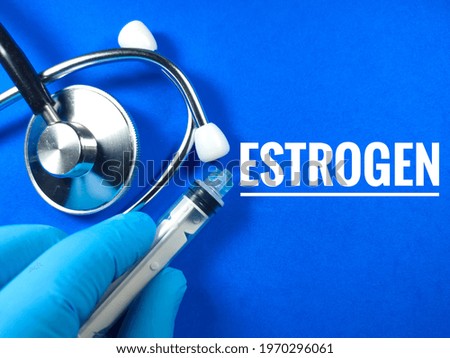 Medical concept.Text ESTROGEN with hand wearing nitrile glove,syringe and stethoscope on blue background.
