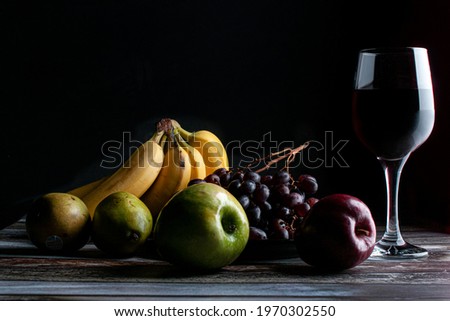 Baroque, renaissance still life fruits on a wooden rustic table with a glass of wine on the side with bananas grapes pears red apple and green apple low key light chiaroscuro dark food Royalty-Free Stock Photo #1970302550