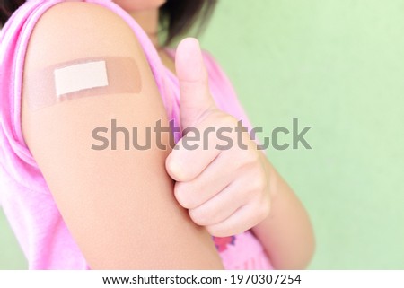 Closeup of shoulder of a vaccinated young Asian girl with adhesive bandage in thumbs up. Young people, children and kids vaccination for covid-19 vaccine.