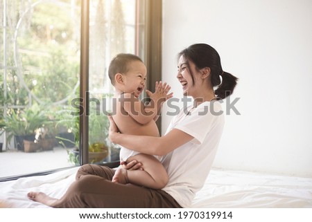 Asian mom smiling happy holding and playing clap hand with her son. Mom and baby in mother’s day concept.