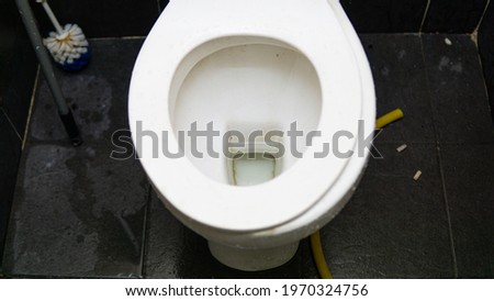 Top view of white toilet bowl with wet floor and cigarette on the floor. Selective focus on foregrounds.