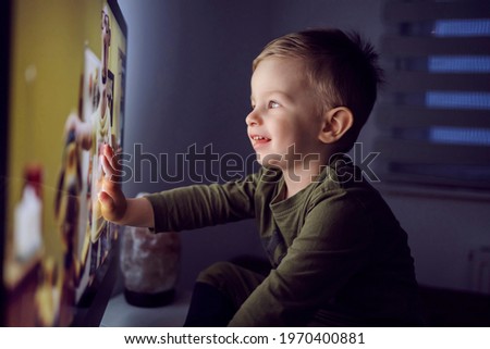 A bedtime ritual for toddlers. The boy touched the TV screen with one hand. A close-up shot of a kid in pajamas sitting right in front of the TV and staring at a cartoon Watching favorite cartoon show