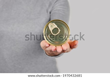 Hand with metal can, preserve tin on grey