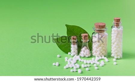 Bottles with homeopathic globules on a green background. Homeopathic medicine. Royalty-Free Stock Photo #1970442359