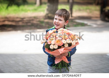 A little boy of four years old smiles and holds a huge bouquet of roses in his hands.