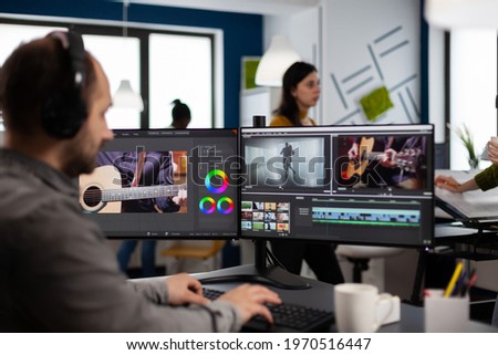 Video maker listening music at headphones editing movie using post production software working in creative agency office. Videographer processing audio film montage on computer in multimedia company