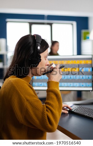 Photo editor with headphones retouching image using stylus pen, drinking coffee, working on PC with two displays. Woman retoucher editing in software app with graphic tablet sitting in creative agency