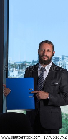Portrait of Confident bearded businessman in black suit with blue folder posing in the office. copy space. Man in confident suit and blue tie. Vertical composition. Long header banner format. 