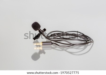 Small lavalier microphone or lapel mic with clip on white background. Professional sound recording equipment for cell phone.