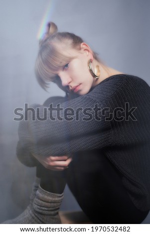 Unhappy attractive caucasian blonde girl in black sweater and perfect make-up sitting with depression emotion face. Loneliness or sad mood concept. High quality vertical photo