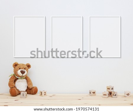 3 blank vertical frames mockup on wall for nursery wall art display, baby room three white frames mock up, wooden shelf, soft toys and wooden toys on shelf. Royalty-Free Stock Photo #1970574131