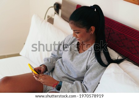 Beautiful African woman sitting on her bed using cell phone
