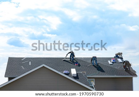 4 construction workers fixing roof against clouds blue sky. Roofer install shingles at the top of the house. Renovate, improve, build home exterior by professional teamwork. Safety, protection concept Royalty-Free Stock Photo #1970590730