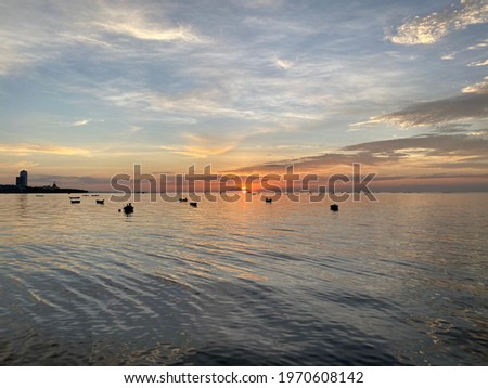 Many small boats are floating in the sea with the orange light from the Sun and clear sky.