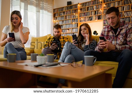A group of friends looking at their smartphones at a boring house party while drinking hot beverages