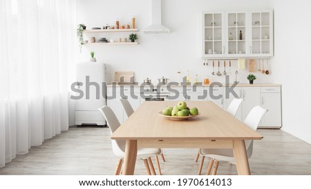 Contemporary minimalist interior of kitchen and dining room. White furniture with utensils and dinner table with chairs in Scandinavian style. Modern light design Royalty-Free Stock Photo #1970614013