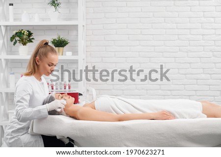 Side view of young beautiful woman lying on procedure for cleaning face with special modern professional equipments. Concept of process care for skin face and body in beauty salon.  Royalty-Free Stock Photo #1970623271