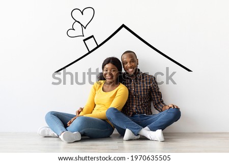 Family Housing. Happy Black Couple Sitting Near White Wall With Drawn Roof, Smiling Young Romantic African American Spouses Imagining Their New Home, Planning Relocation, Creative Collage Royalty-Free Stock Photo #1970635505