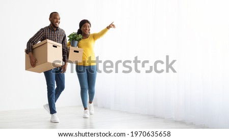 Happy Black Couple Walking With Cardboard Boxes In Their New Apartment, Planning Where To Place Furniture, Young African American Spouses Unpacking After House Relocation, Panorama With Copy Space Royalty-Free Stock Photo #1970635658