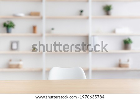 Workplace of employee, blogger, doctor in clinic or home office. Wooden table and chair, nobody. Shelf with plants in pots and decorative elements, on white wall background, in daylight, empty space
