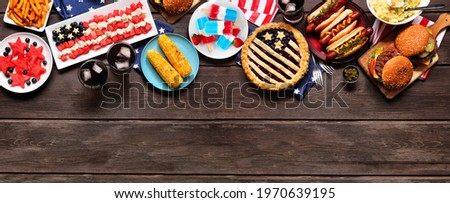 Fourth of July, patriotic, American themed food. Overhead view top border on a dark wood banner background. Copy space.